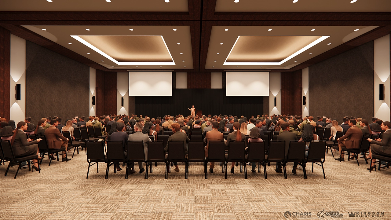A modern conference hall filled with attendees seated in rows, facing a speaker on stage. The room features warm lighting, a neutral color scheme, and large projection screens on the edges of the stage.