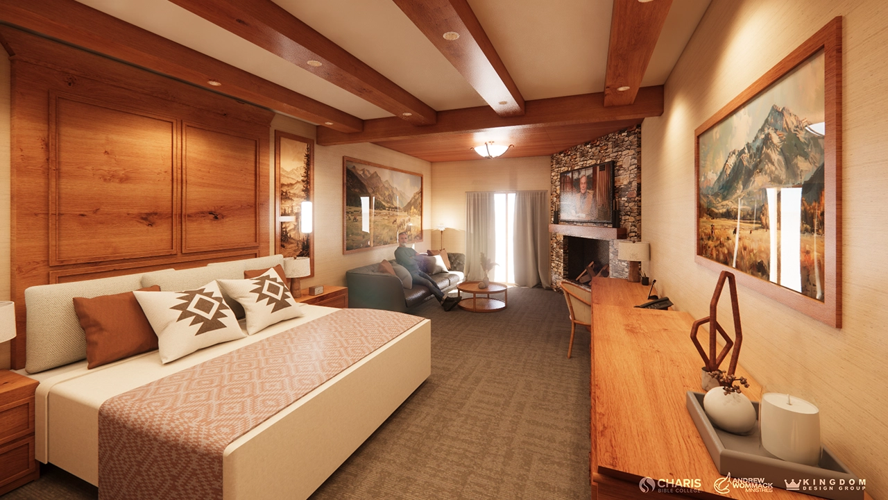 A warm, rustic hotel room featuring a large bed with decorative pillows, wooden beams, and mountain-themed artwork. The space includes a cozy seating area by a stone fireplace with a TV, a writing desk, and a sliding door leading to a balcony.