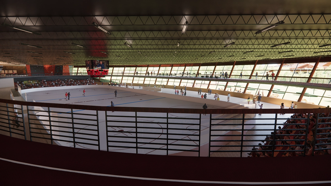 A large indoor sports arena with a central rink, surrounded by spectator seating and an elevated walkway with additional viewing areas. Players are on the rink, while a crowd watches from the stands. The arena features a high ceiling with industrial lighting, large windows allowing natural light, and a digital scoreboard displaying game details.